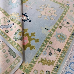 May include: A detailed shot of a light blue and pink rug with a floral design and a green border. The rug features a traditional pattern with intricate details. The text "sameeara handcraft" is visible.