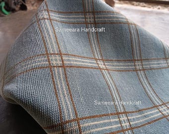 May include: A folded blue rug with a plaid pattern in brown and white. The rug is made of a textured material and is labeled "Sameeara Handcraft". The rug is on a concrete surface.