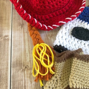 以下が含まれることがあります： 赤ちゃん用の手編みの帽子セット。セットには、黄色とオレンジのタッセルが付いた赤いカウボーイハット、黒いアイパッチが付いた白い帽子、茶色とベージュの帽子が含まれています。