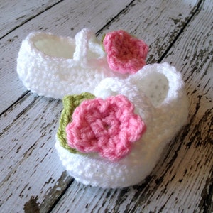 May include: A pair of white crocheted baby shoes with pink and green flower embellishments.