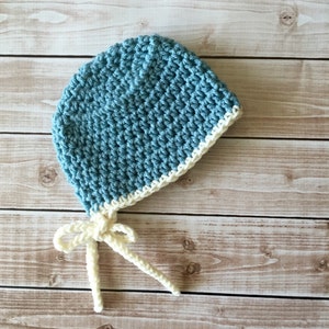 May include: A blue crocheted baby hat with a white crocheted brim and matching ties.
