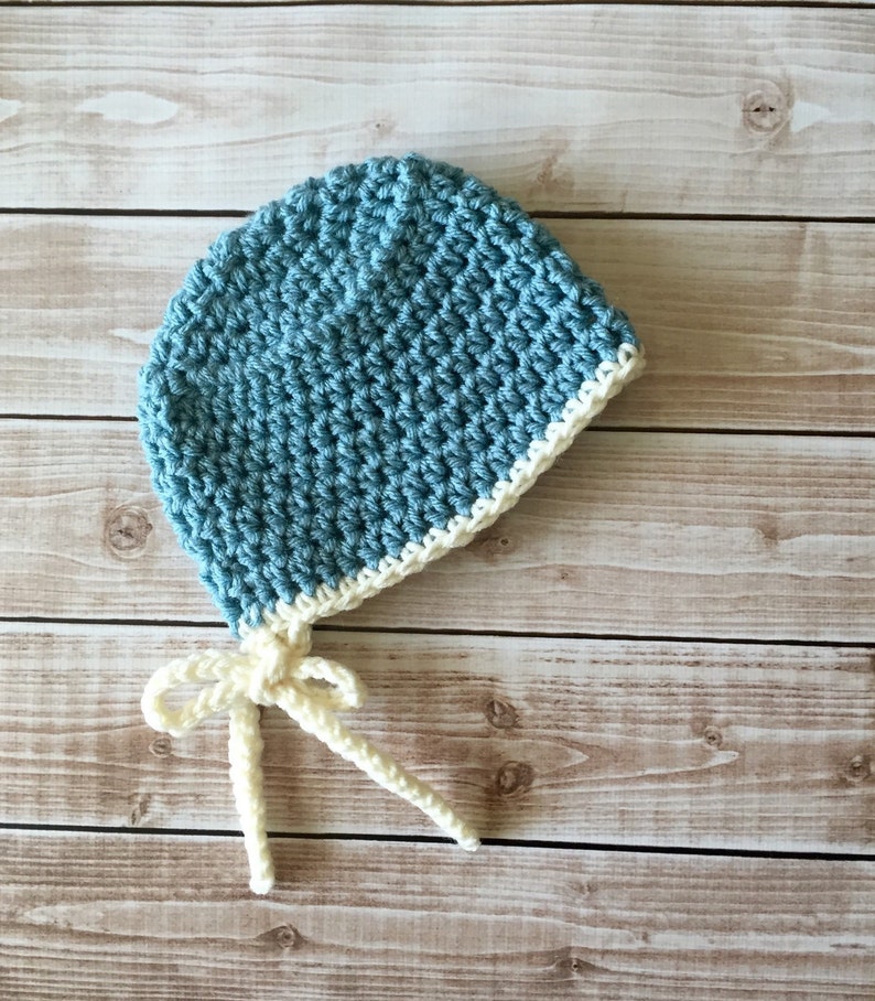 May include: A blue crocheted baby hat with a white crocheted brim and matching ties.