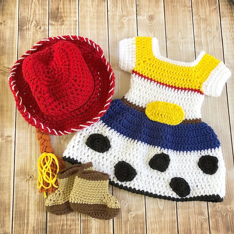 以下が含まれることがあります： 赤色のカウボーイハット、茶色のブーツ、白、青、黄色の黒のドット柄のドレスが付いた、赤ちゃんまたは幼児用のクロシェ編みのコスチュームセット。ドレスは、トイストーリーのキャラクター、ジェシーからインスピレーションを得ています。