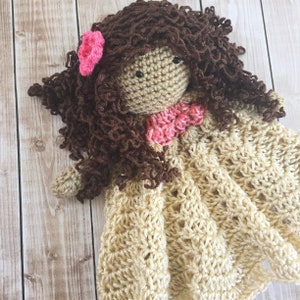 Pode incluir: Boneca de croch&ecirc; com cabelo castanho encaracolado, uma flor rosa e um vestido de croch&ecirc; rosa e branco.