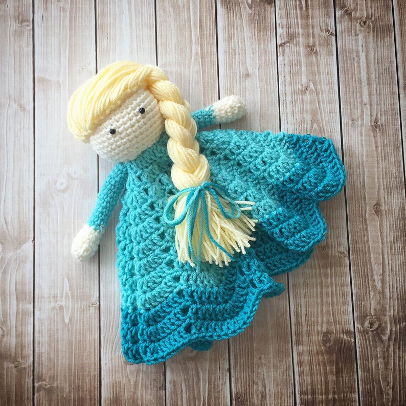 May include: A crocheted doll with blonde hair and a blue and green dress. The doll is wearing a blue and green crocheted dress with a yellow crocheted braid.
