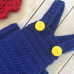 Pu&ograve; includere: Salopette in crochet blu con bottoni gialli. La salopette &egrave; realizzata con un punto testurizzato e ha un design classico di salopette.