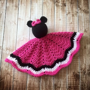 May include: A pink, black, and white crocheted baby blanket with a black crocheted Minnie Mouse head attached.