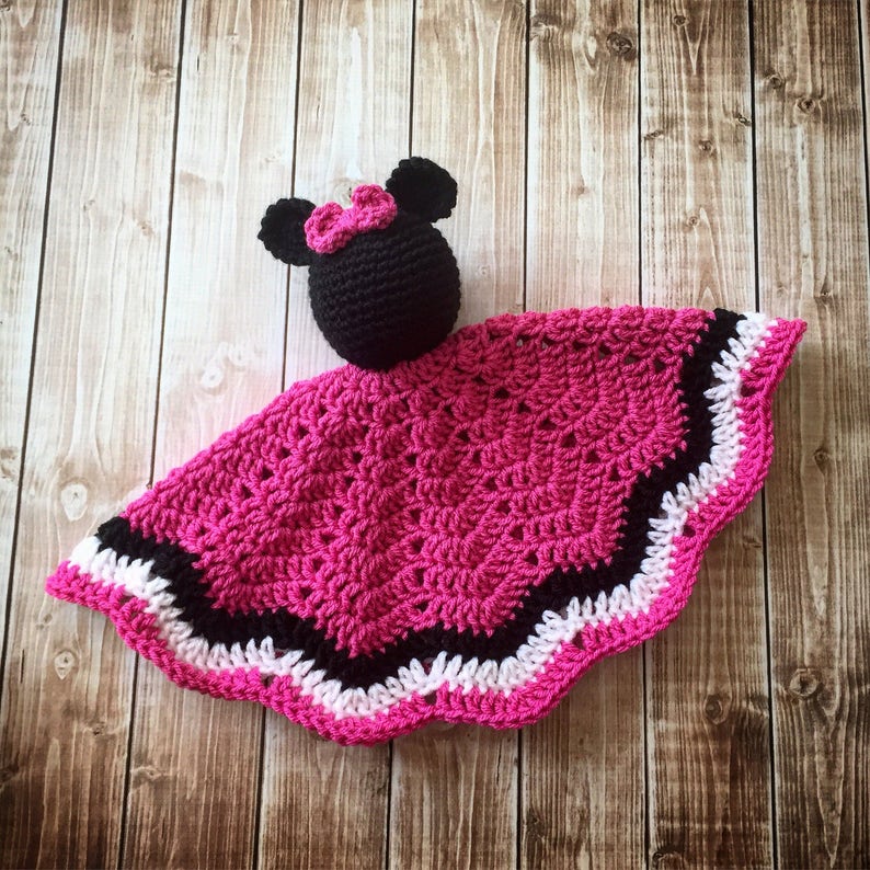 May include: A pink, black, and white crocheted baby blanket with a black crocheted Minnie Mouse head attached.