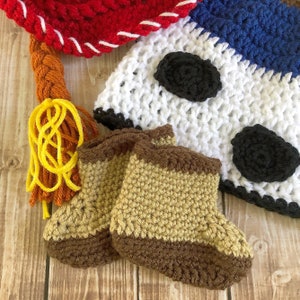 以下が含まれることがあります： 茶色とベージュの2つのクロシェ編みのベビーブーティと、黒のアクセントが付いた白と茶色のクロシェ編みの帽子