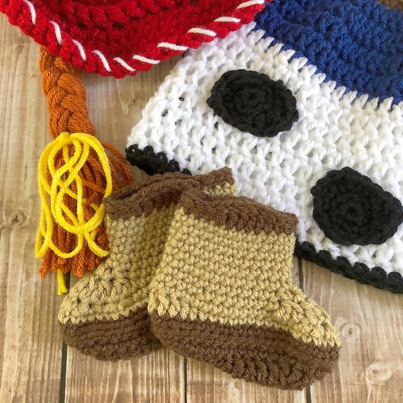 以下が含まれることがあります： 茶色とベージュの2つのクロシェ編みのベビーブーティと、黒のアクセントが付いた白と茶色のクロシェ編みの帽子