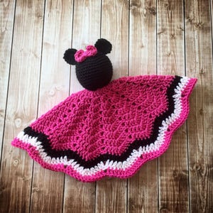 May include: A pink, black, and white crocheted baby blanket with a black crocheted Minnie Mouse head attached.