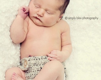 May include: A sleeping baby wearing a crocheted diaper cover with a button closure. The baby is lying on a white fluffy blanket.