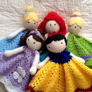 May include: Five crocheted princess dolls with blankets. The dolls are dressed in their signature colors: blue, purple, red, white, and green.