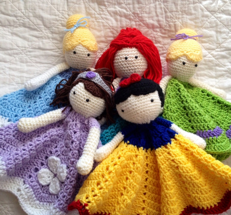 May include: Five crocheted princess dolls with blankets. The dolls are dressed in their signature colors: blue, purple, red, white, and green.