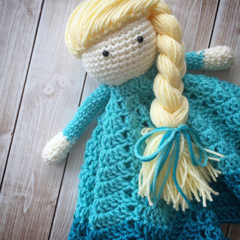 May include: A crocheted doll with long blonde yarn hair wearing a blue and teal crocheted dress.