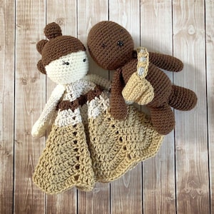 May include: A crocheted blanket with a brown and white crocheted doll and a brown crocheted character. The doll is wearing a brown and white dress and the character has a brown and white strap.
