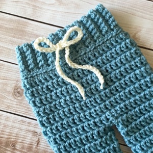 May include: Blue crocheted baby trousers with a white crocheted drawstring.