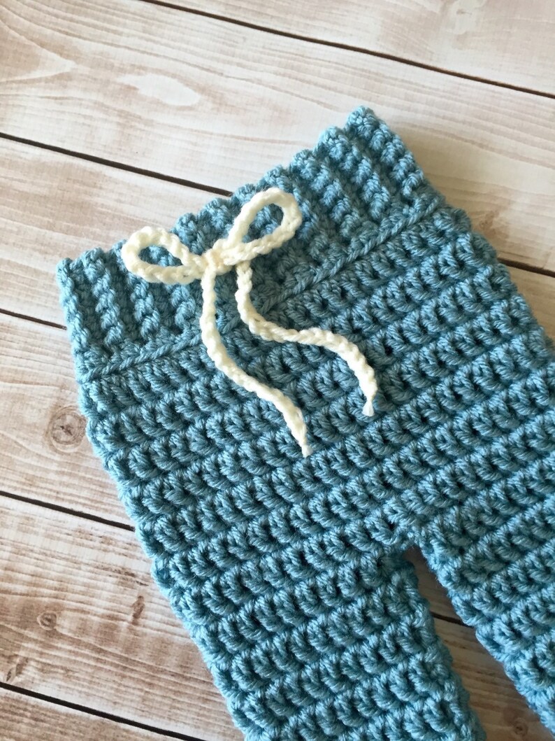 May include: Blue crocheted baby trousers with a white crocheted drawstring.