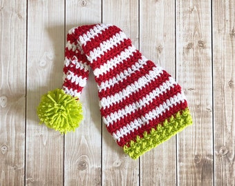 May include: A red and white striped crocheted elf hat with a green pom-pom on top.