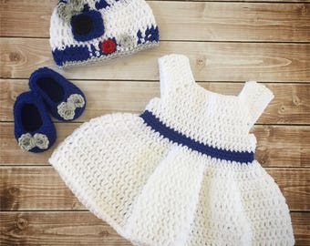 May include: A white crocheted dress with a blue crocheted waistband, a white crocheted hat with blue and gray details, and two pairs of blue crocheted booties with gray flower accents.