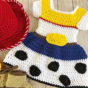 以下が含まれることがあります： トイストーリーのキャラクター、ウッディをモチーフにした、かぎ針編みベビーワンピース。ワンピースは白地に青、黄、茶色のアクセントが施されています。胸には黄色の星形のワッペン、茶色のベルトには黄色のバックルが付いています。ワンピースは黒い水玉模様で飾られています。