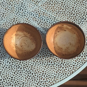 May include: A set of three ceramic mugs with a speckled, matte finish. The mugs are in shades of cream, light gray, and dark gray. Each mug has a simple, minimalist design and a rounded handle.