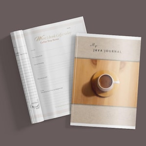 Op de afbeelding: Een koffiejournaal en een open notitieboek met gelinieerde pagina's worden weergegeven op een bruin oppervlak. De kaft van het journaal bevat de tekst "MT JAVA JOURNAL" en een koffiekopje op een houten onderzetter. Het open notitieboek heeft de tekst "Where I drink coffee today Coffee Shop Review".