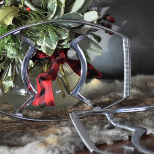 May include: A silver metal serving stand with a decorative design. The stand is on a brown and white faux fur surface.