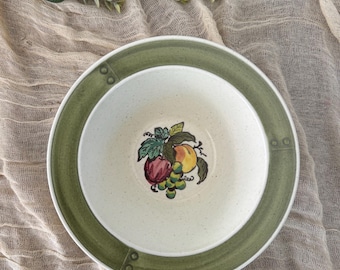May include: A white ceramic bowl with a green rim and a fruit design. The bowl has a speckled glaze and a raised rim.