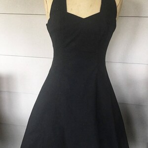 May include: A black halter dress with a fitted bodice and a flared skirt. The dress is on a mannequin.