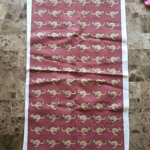 May include: A rectangular linen tea towel with a repeating pattern of tan kangaroos on a burgundy background. The towel has a white border and text that reads "designed and printed on pure linen in Australia" and the name "Rodriguez".