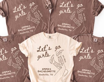 May include: Five t-shirts, in ivory and espresso colors, are displayed. Each shirt features the text "Let's go girls" with a graphic of cowboy boots and the text "EMMA'S BACHELORETTE Nashville, TN".