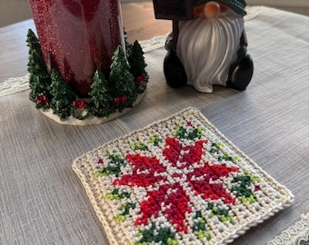May include: A red glitter pillar candle with a base of miniature green Christmas trees. A crocheted square coaster with a red and green floral design sits next to a gnome figurine wearing a green hat and holding a sign.