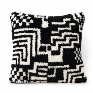 Peut inclure: Coussin carré noir et blanc avec un motif géométrique. Le motif est composé de lignes blanches épaisses formant un motif répétitif sur un fond noir. Le coussin a une texture duveteuse et est probablement fait d'une matière douce et moelleuse.
