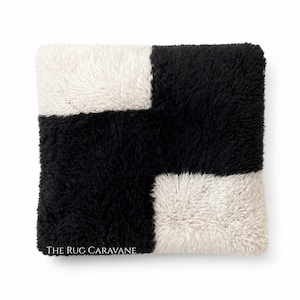 Peut inclure: Tapis carré et moelleux avec un motif géométrique. Il est divisé en quatre sections avec des carrés noirs et blanc cassé en alternance. La texture semble douce et pelucheuse. Le texte "THE RUG CARAVANE" est imprimé en bas.