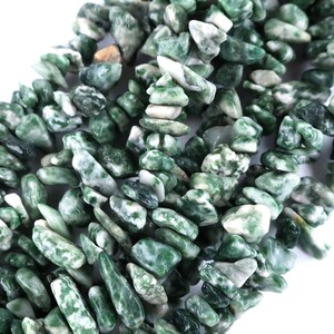 May include: A collection of small, tumbled stone chips in varying shades of deep forest green and opaque white. The stones have irregular, angular shapes and smooth, polished surfaces, creating a dense, textured pile of natural mineral fragments.