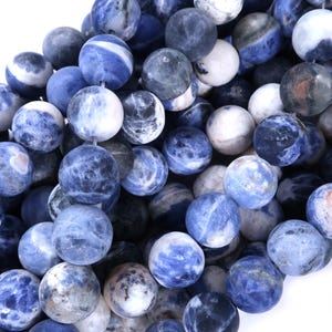May include: A collection of round, blue sodalite gemstone beads. The beads vary in shades of blue, with white marbling and patterns. These beads are suitable for jewelry making, such as necklaces and bracelets.