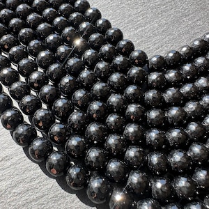 May include: Close-up of a strand of faceted black beads. The beads have a shiny, reflective surface and are arranged in a curved pattern. The beads are likely used for jewelry making or crafting.