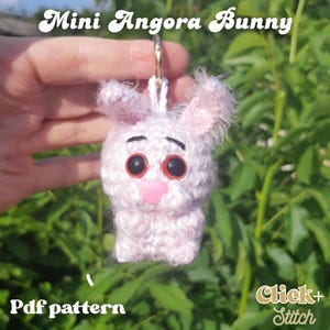 May include: A light pink, crocheted bunny keyring with large, red-rimmed eyes and a pink nose. The keyring has a gold ring and the text "Mini Angora Bunny" is above the bunny. The text "Pdf pattern" is below the bunny.