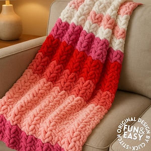 May include: A handmade, chunky knit blanket in shades of pink, red, and white, draped over a beige armchair. The blanket features a textured, heart-shaped pattern. The words "Original Design by Click + Stitch Fun & Easy" are in the lower right corner.