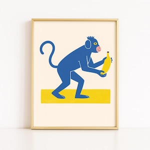 May include: A framed art print featuring a blue monkey holding a yellow banana. The monkey stands on a yellow rectangle against a cream background. The print is in a gold frame.