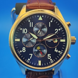 May include: A gold-toned wristwatch with a dark blue face and a brown leather band. The watch features multiple sub-dials, luminous hands, and the text "BOTZHE 1986". The watch has a date display at the 3 o'clock position.