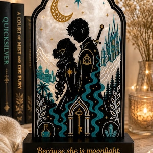 May include: An arched decorative display featuring a black silhouette of two figures facing each other, surrounded by teal and gold illustrations of a castle, moon, stars, and a key. The black base bears the text, Because she is moonlight.