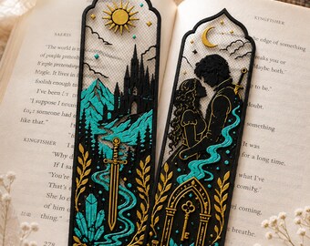 May include: A set of two 3D printed bookmarks featuring intricate black, gold, and teal designs. One bookmark displays a sun, castle, mountains, and a sword. The other shows a crescent moon, two figures, a key, and a mortar and pestle.