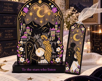 May include: An arched wooden display piece and a matching bookmark featuring a couple in front of a castle under a crescent moon and stars. The display base is inscribed with the text 'To the stars who listen' in purple lettering on a black background.