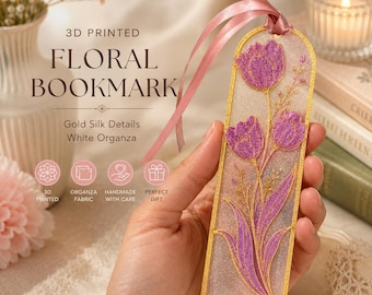 May include: A 3D printed bookmark featuring a translucent white base with embedded purple floral designs and gold silk outlines. The rectangular bookmark has a rounded top edge and is finished with a light pink ribbon attached at the top.