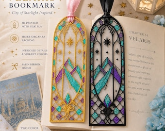 May include: Two arched bookmarks featuring intricate lattice designs with mountain motifs, one in gold and one in black. Both bookmarks have sheer organza backing, vibrant teal and purple accents, and are topped with satin ribbons in pink and black.