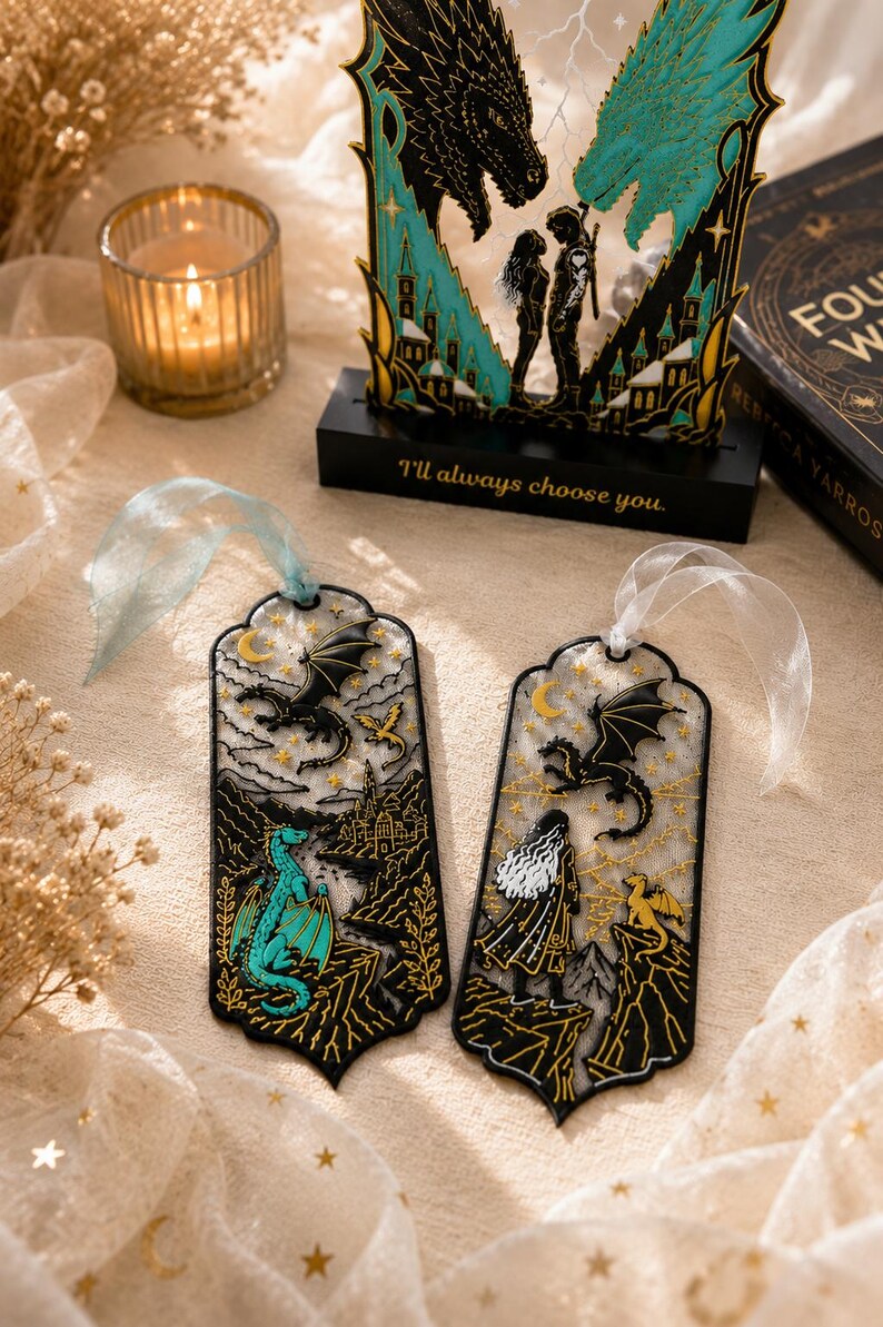 May include: Two rectangular bookmarks with rounded edges and ribbons, featuring black outlines, gold stars, and dragon illustrations. One bookmark shows a teal dragon, the other a person with long hair and a small yellow dragon. Both have intricate mountain scenes.
