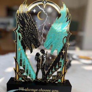 Dragon book stand with two matching Fourth Wing inspired bookmarks displayed on a reading table beside a fantasy book.
