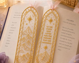 May include: Two rectangular bookmarks with gold embroidered mountain and star designs on white organza fabric. One bookmark features the text "TO THE STARS WHO LISTEN AND THE DREAMS THAT ARE ANSWERED" in gold thread. Both have pink ribbon toppers.